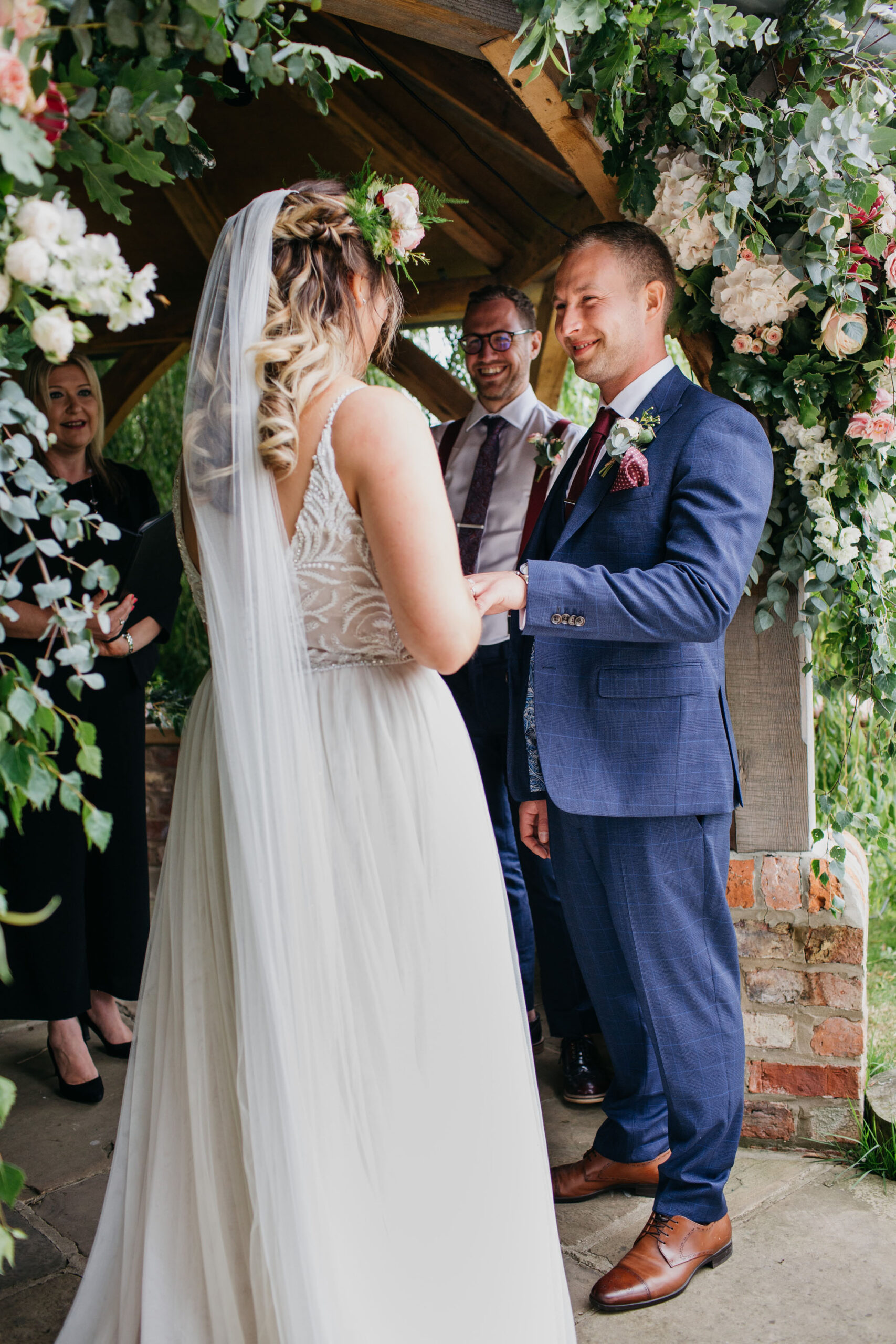 Yorkshire wedding photography of Alicia and Phil. She wears a white boho style dress and he's in a blue ckech suit. She has a full flower crown in delicate pinks, and they look happy. Image by John Hope Photography